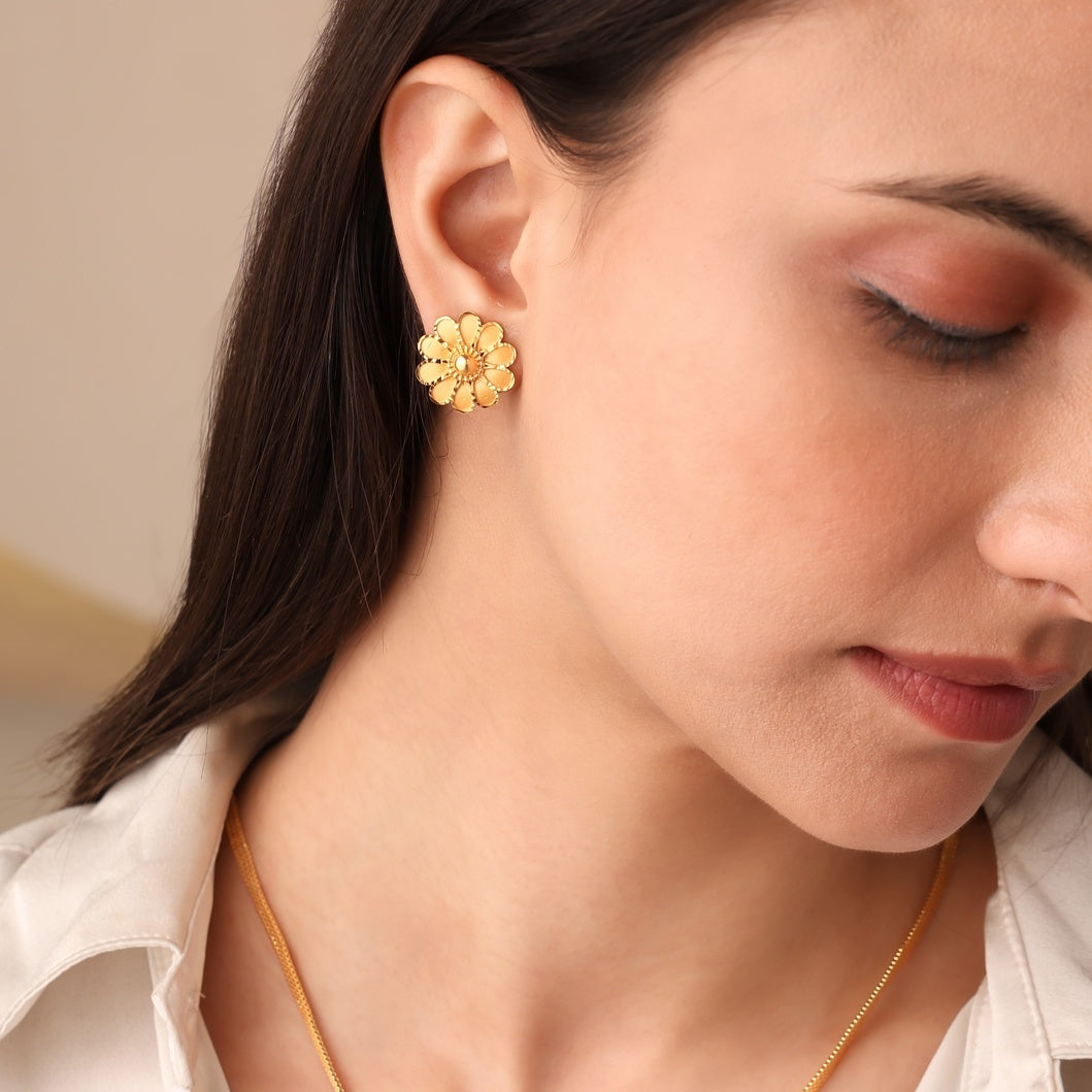 Woman wearing gold floral earrings and necklace against a neutral background