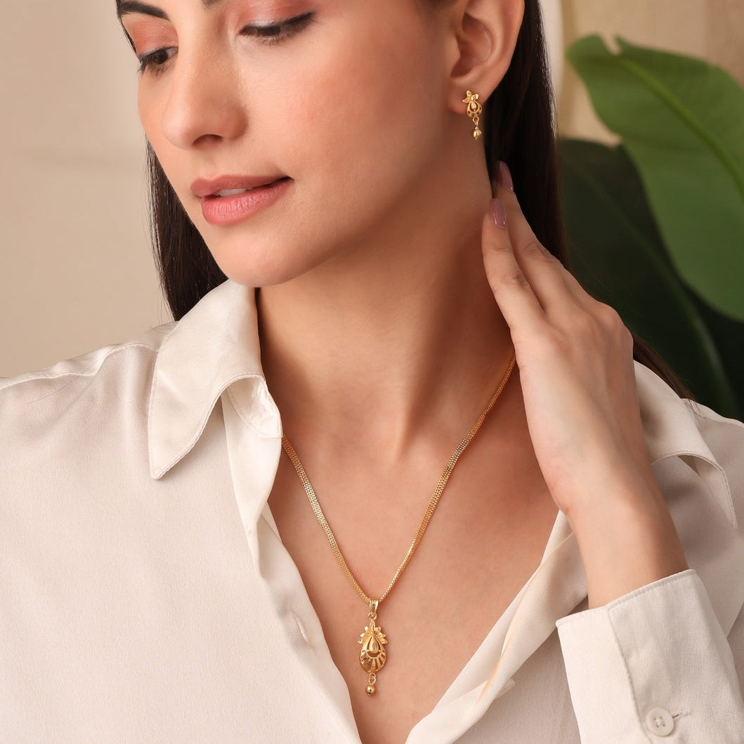 Woman wearing gold jewelry, including a necklace and earrings, against a neutral background.