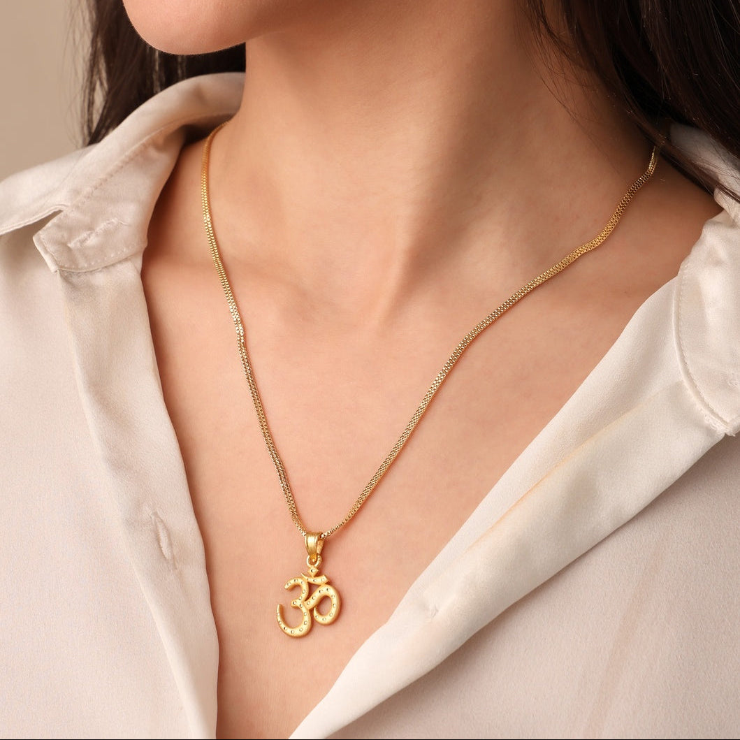 Woman wearing a gold necklace with an Om symbol on a neutral background