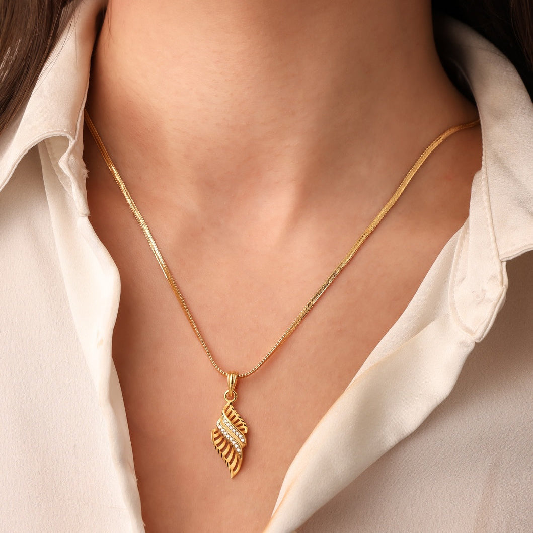 Gold necklace with a leaf pendant worn by a person in a white shirt.