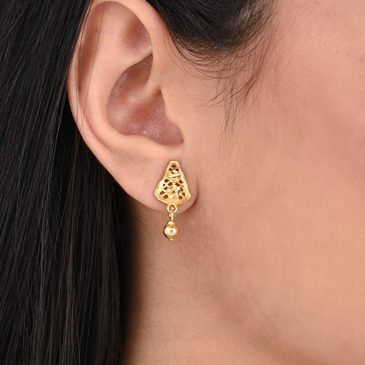 Gold earring worn by a person with dark hair