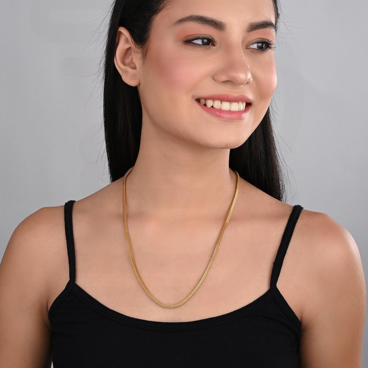 Woman wearing a gold necklace against a gray background