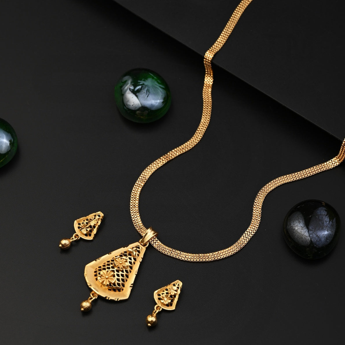 Gold necklace and earrings on a dark surface with green stones.