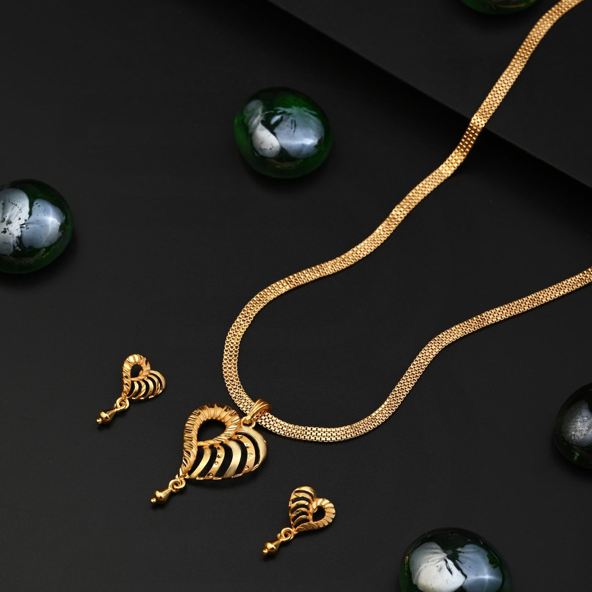 Gold necklace with heart-shaped pendants on a dark surface with green stones.