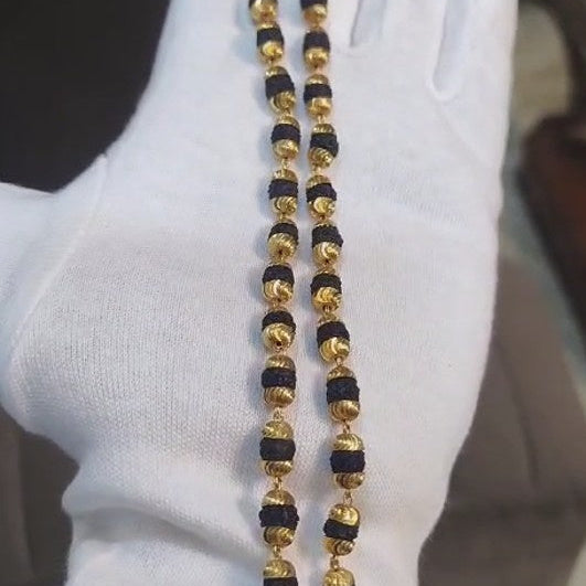 Gold and black beaded necklace held by a gloved hand against a neutral background