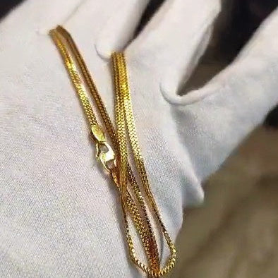 Gold chain held by a gloved hand against a neutral background