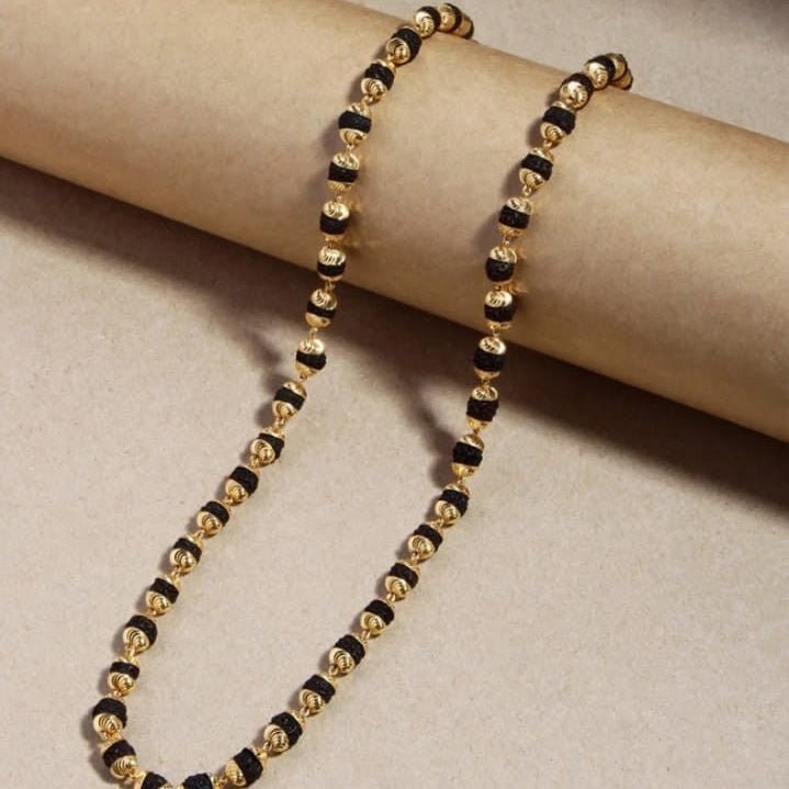 Gold and black beaded necklace on a beige surface